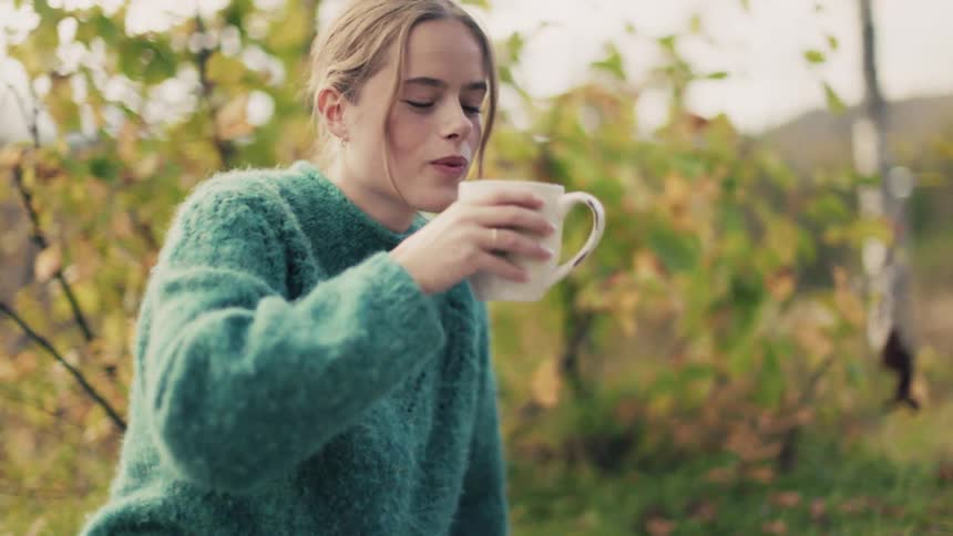 Woman sitting on the grass picking up a cup and drinking from it