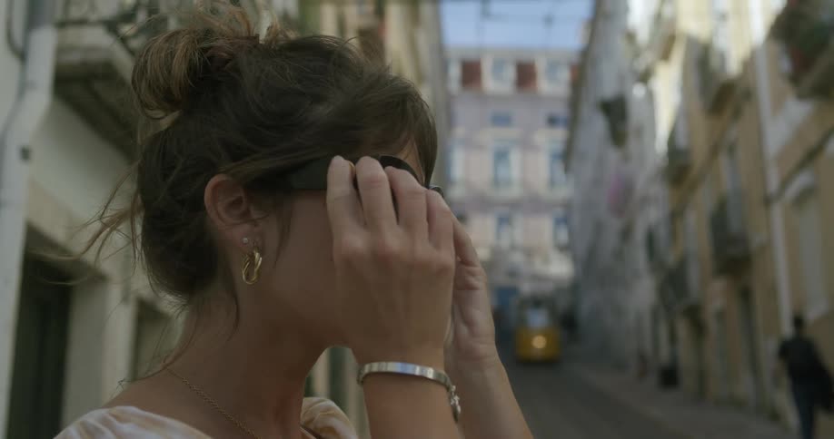 Close up of the face of a woman wearing sunglasses on a street with classic european architecture
