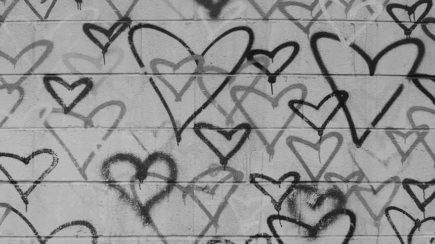 Many graffiti hearts in various shades of gray and black cover the exterior wall of a building