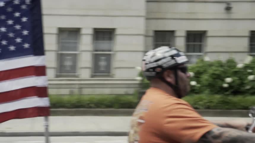 Moving view of a city street with a motorcycle passing by with the us flag