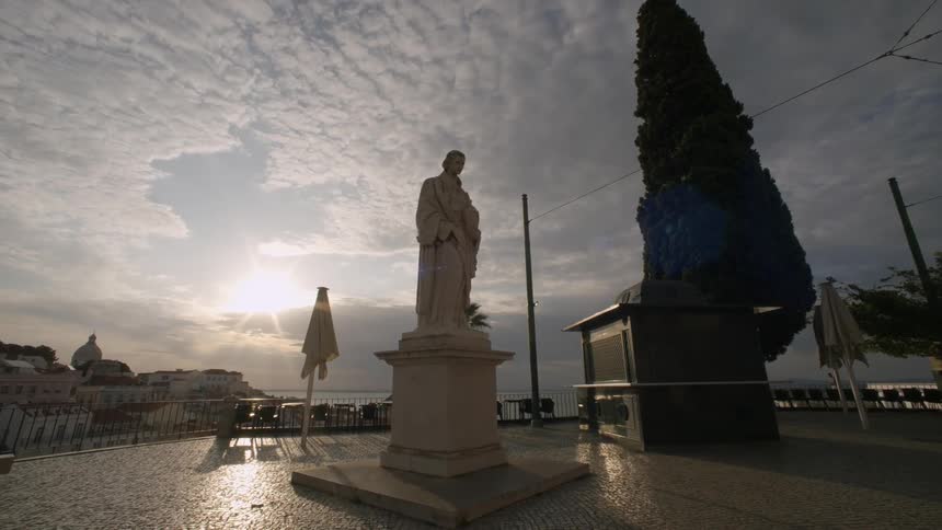 Statue in a square and in the background an urban city with the sun on the horizon