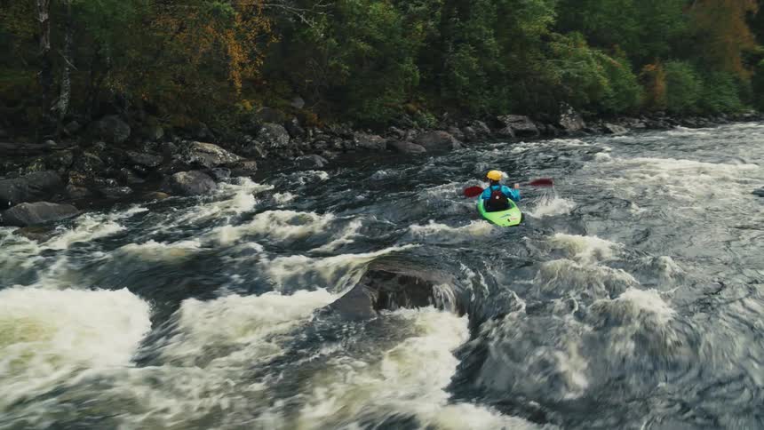 A kayaker navigates through swift rapids surrounded by rocky shores and a forest with autumncolored trees