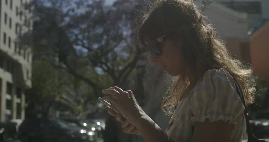 A woman on a city street checking her phone while a light wind blows on her hair
