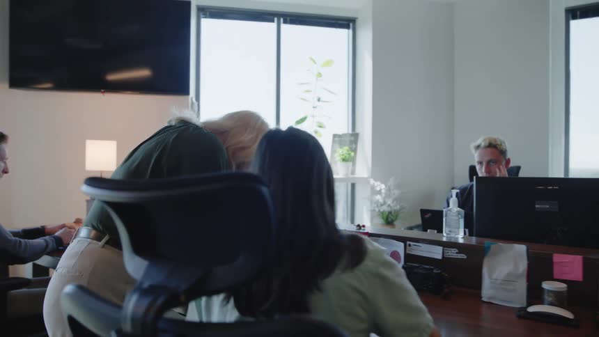 A group of individuals in an office setting seated at desks with computer monitors