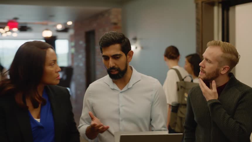 Group of people exiting an elevator collaborate and look at a laptop in an office