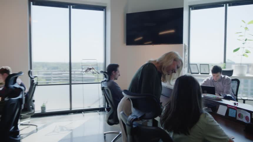Office environment with men and women working sitting and standing with laptops