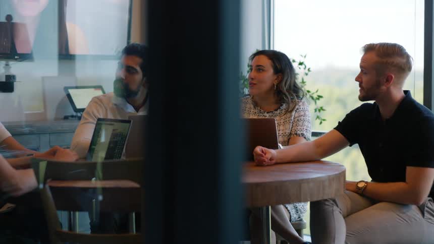 Coworkers hold a meeting while a large screen shows another person attending virtually