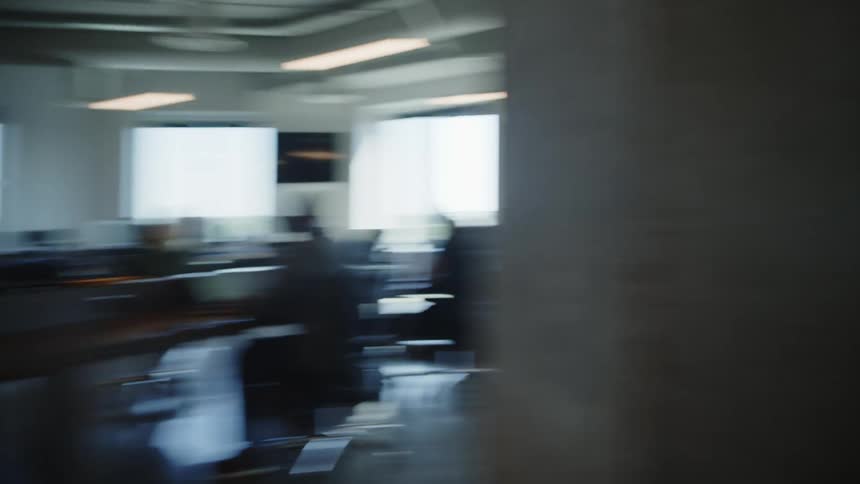 Woman walks into an office pushing a cart with a box of copy paper and coworkers collaborate over computers
