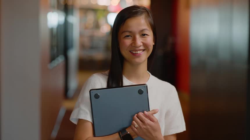 Smiling woman holding a laptop while standing in a hallway