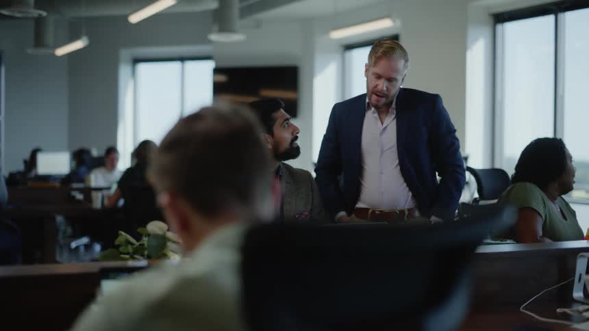 Two men talking in an office surrounded by other people working