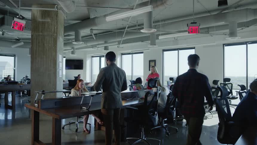 Man walks into an office space and places laptop on a standing desk and opens it