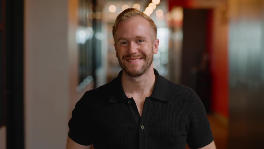 Man in black shirt smiling in a hallway