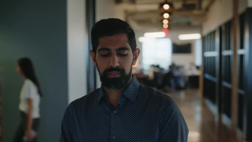 Bearded man with a laptop walking down an office corridor