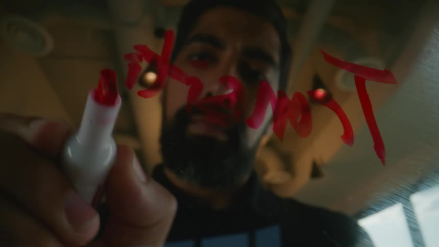 Man with beard writing with a red dry erase marker on a transparent board