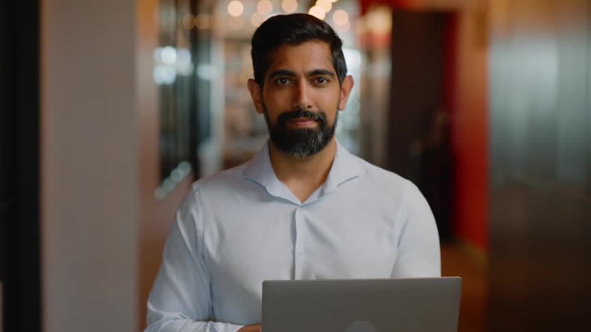 Man stands in a hallway holding an open laptop