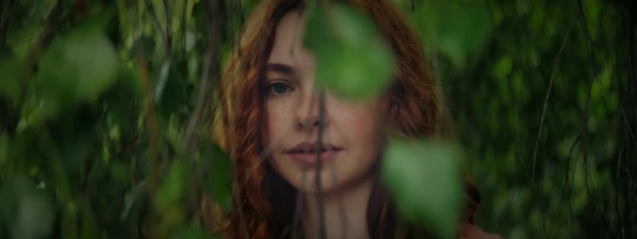 Portrait of a young redhaired woman among green leaves