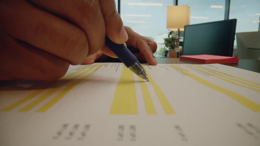 A hand uses a pen to mark up a paper with graphics on a desk