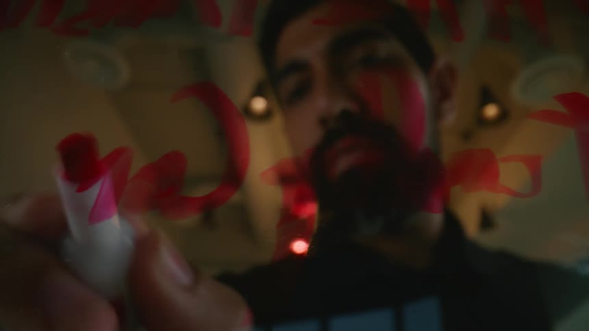 Bearded man writing with a red marker on a glass