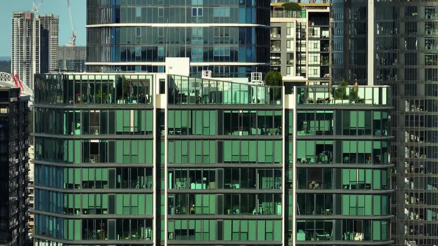 Modern building with green glass facade and balconies with plants and other buildings in a metropolis
