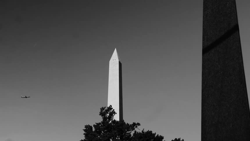A monochrome view of an airplane flying behind the washington monument