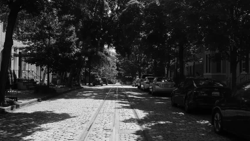 Treelined street with cars parked on both sides and tram tracks in the center