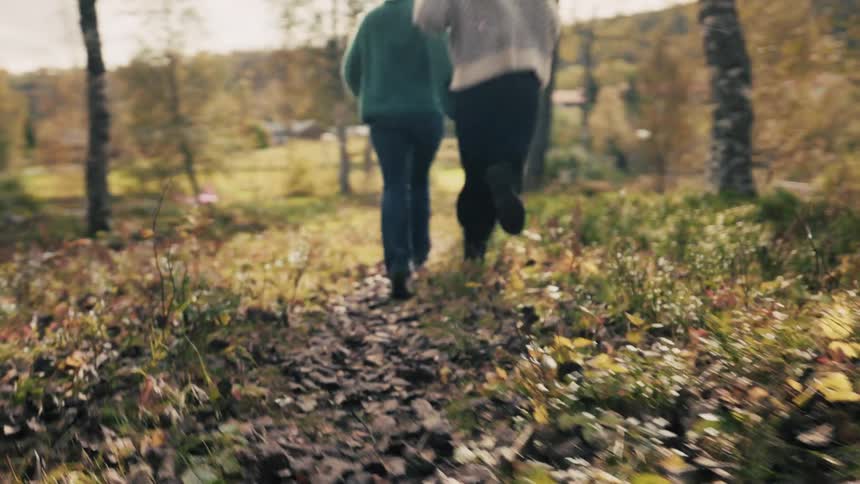 Two women holding hands running down a trail with trees around them