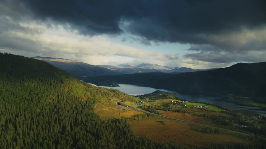 Landscape view of a valley with a river running through it surrounded by mountains and patches of sunlight breaking through an overcast sky