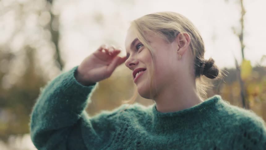 Side view of a young blonde woman with a happy facial expression fixing her hair