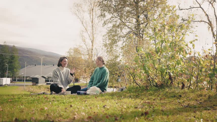 Two women sitting on the grass facing each other talking