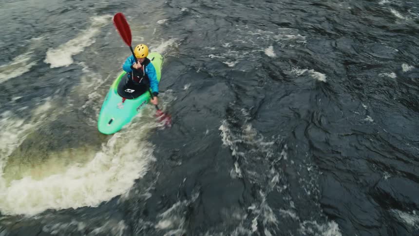 Individual kayaking on a river with rapid currents surrounded by rocky banks