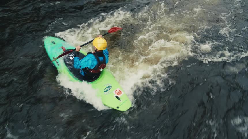 A person in a blue and green kayak navigates rapid river waters wearing a blue jacket and a red helmet