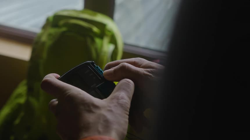 A pair of hands holding a small device with a green backpack in the background