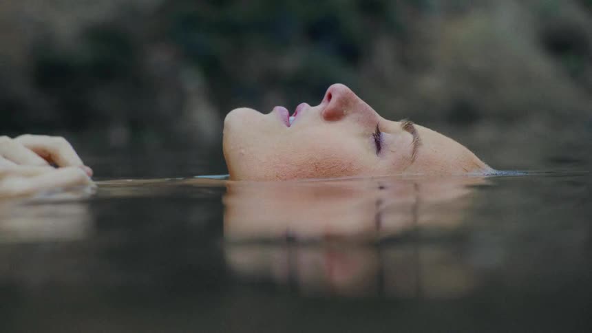 A woman floats in a body of water where you can only see her face and hands