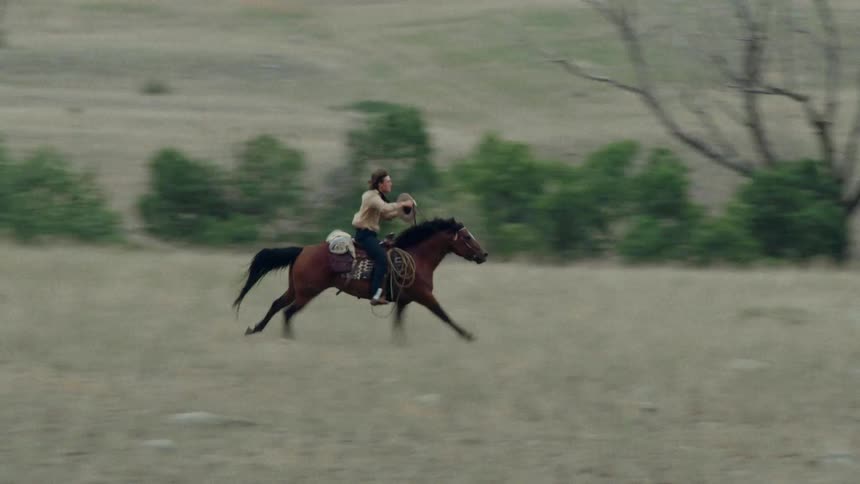 A cowboy rides a horse across a grassy plain