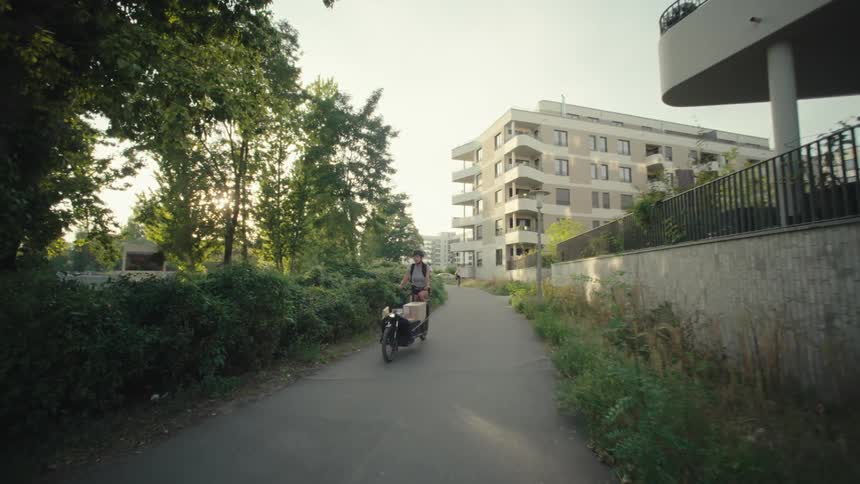 Delivery girl wearing a helmet a gray shirt and shorts rides the cargo bike down the street