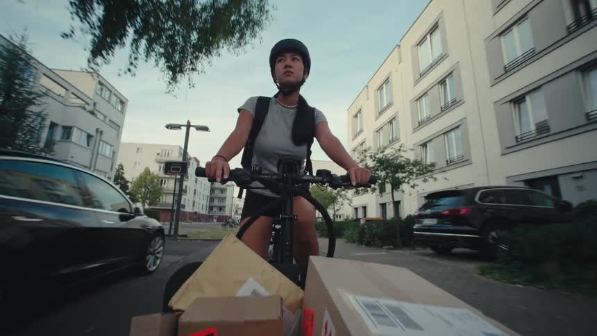A person riding a cargo bicycle on a treelined sidewalk in the city