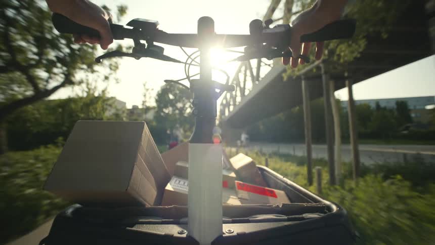 Hands on an electric scooter moving down a street carrying delivery boxes POV