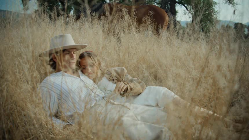 Couple between a man and a woman lying in a field with tall dry grass and in the background a horse