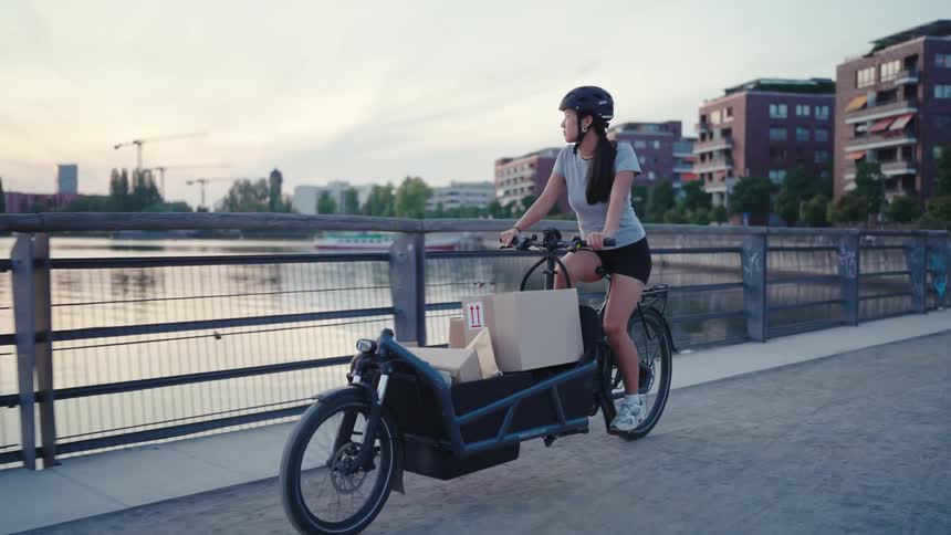 Woman pedals cargo bicycle across a bridge near apartment buildings