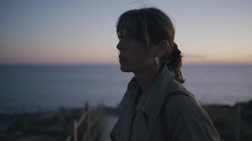 A woman stares out at the ocean as the sun sets