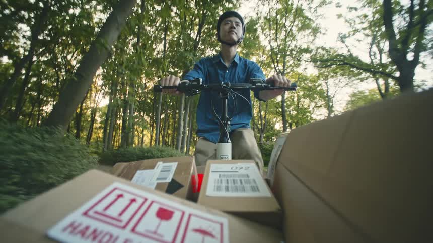 Package delivery worker pedals cargo bicycle through the park POV