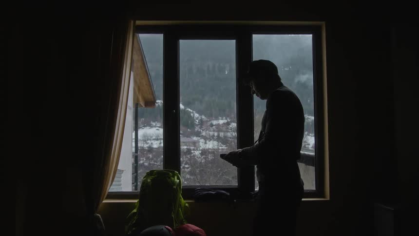 Man stands indoors near a window overlooking a snowy mountain tying a belt around his chest and waist