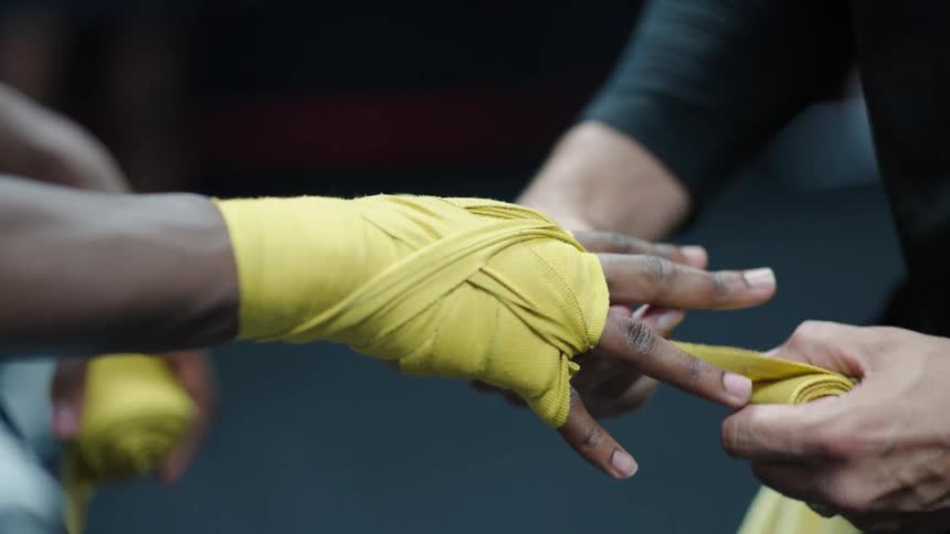 Two hands wrapping a yellow boxing bandage around a boxers wrist