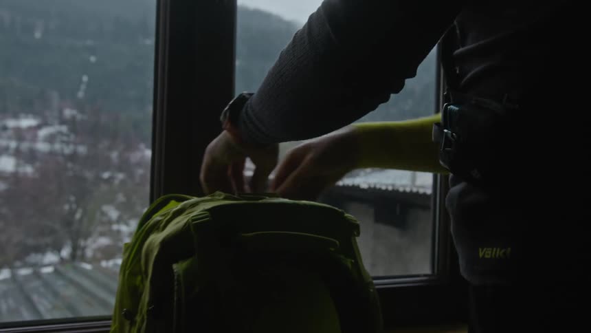 A man quickly packs his backpack while indoors near a snow covered mountain