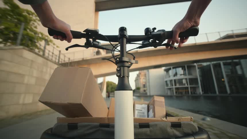 Person riding a cargo bike loaded with boxes near a canal in the city POV