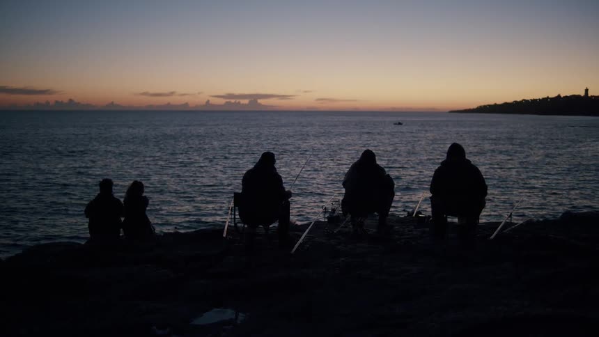 People silhouetted against the water fish on the shore under a red tinted sky