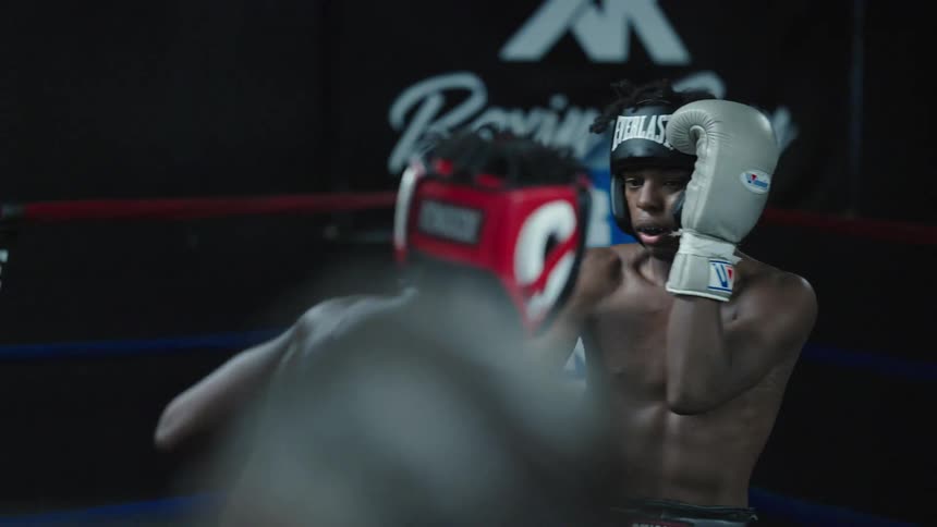 Two young men wearing gloves and head gear box while in a boxing ring