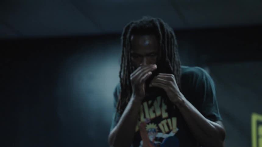A man with long dreadlocks in an intense focused moment shadowboxing with his hands up near his face in a dimly lit indoor setting