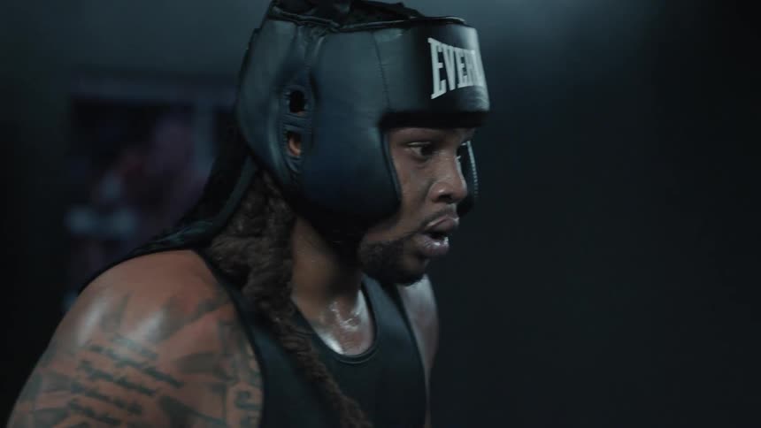 A boxer wearing a black everlast headgear and a sleeveless shirt sweating and appearing focused in the middle of a training session