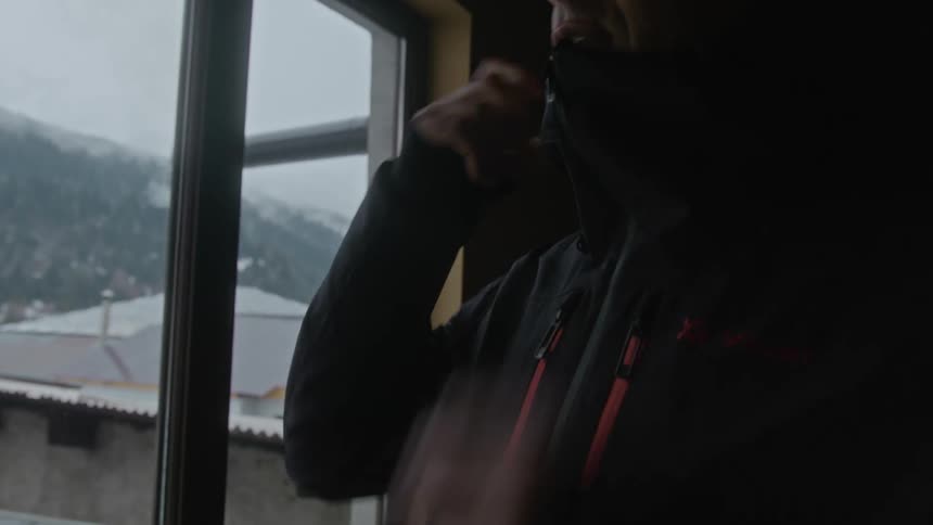 A man zips his coat up in a room